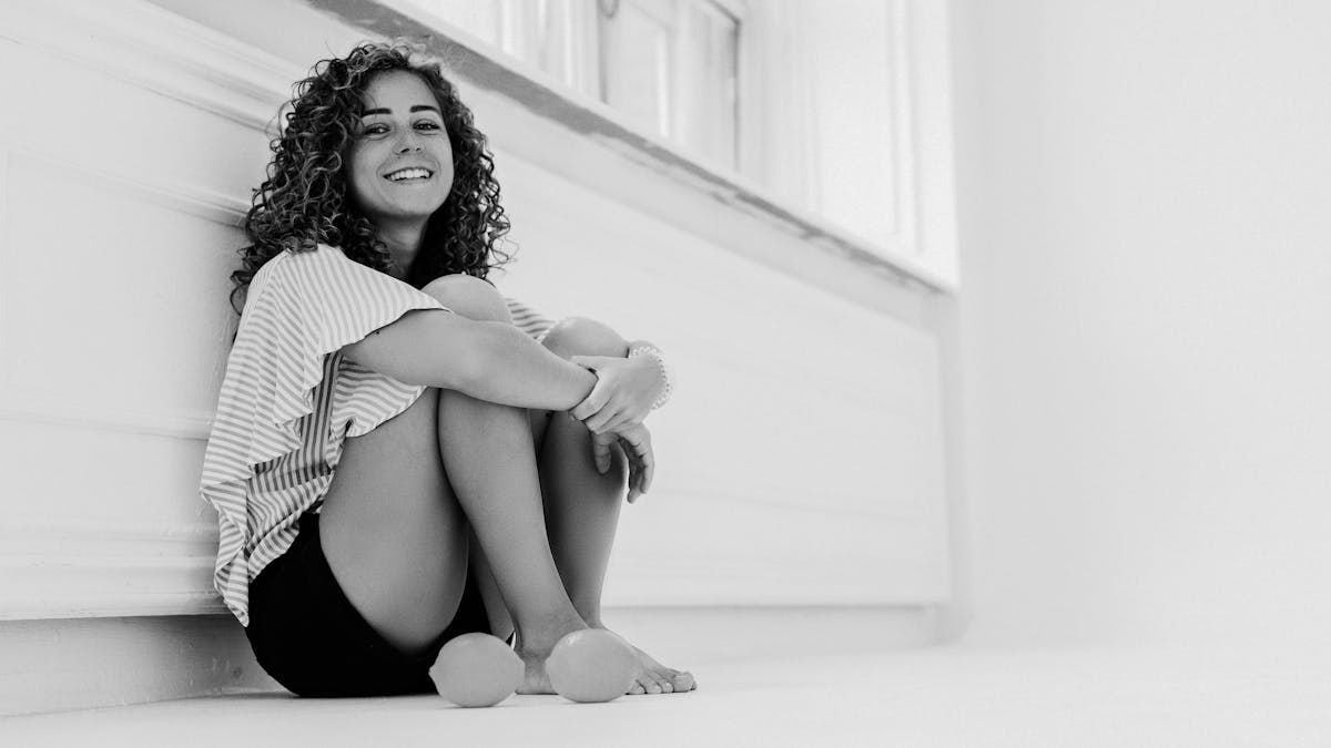 Black and white photo of a woman sitting against a wall, smiling warmly.