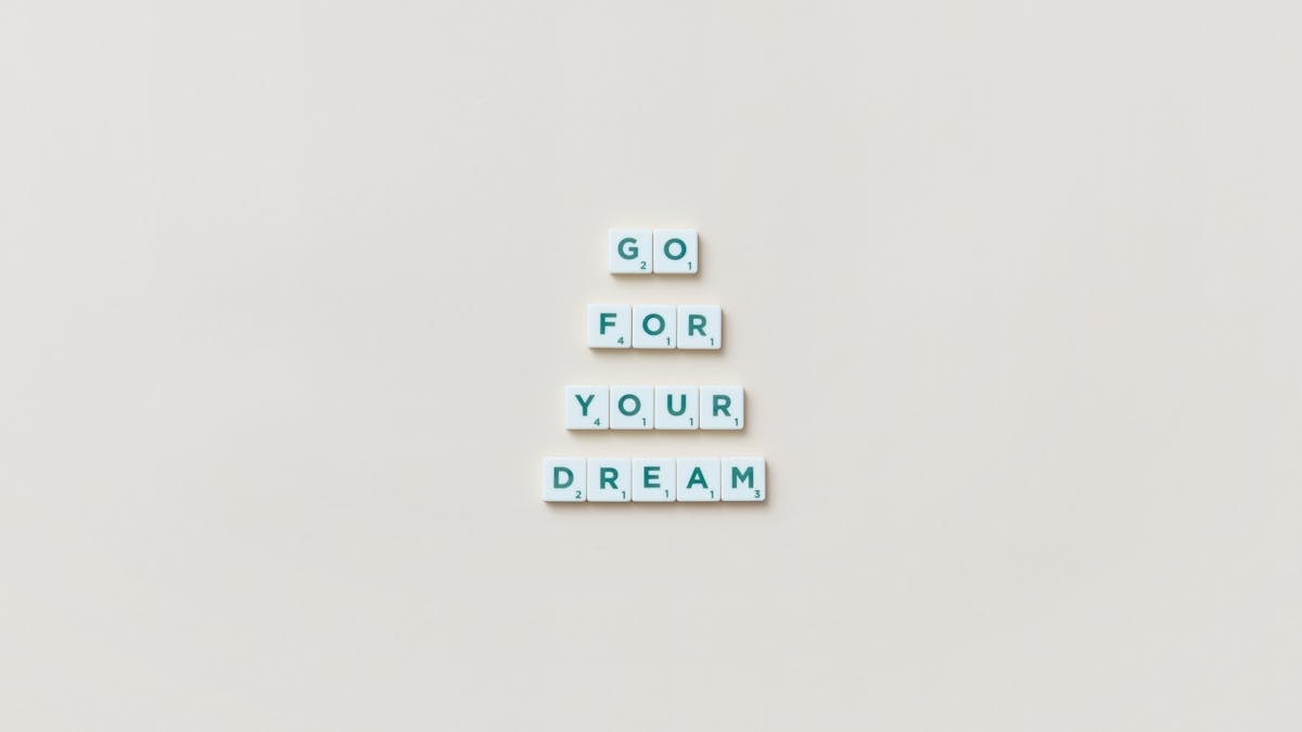 Inspirational text 'Go For Your Dream' made from Scrabble tiles on a plain background.